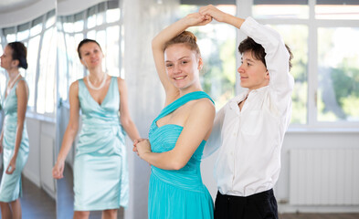 Couple of teenagers in festive clothes learn to dance latin american dance Bachata in studio under...