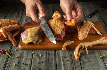 Two hands skillfully chop raw chicken parts on a wooden cutting board in a rustic kitchen setting,...