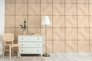 Comfortable wooden chair with chest of drawers and floor lamp near beige tile wall