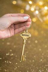 Hand handing over the key to success on a blurred golden background.