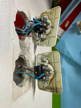 CLOSE UP: Two unplugged old electrical outlets attached to the wall with visible blue wires. Sockets are exposed and partially installed, revealing internal wiring and unfinished installation work.