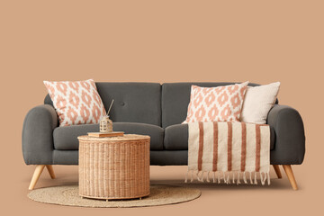 Cozy black sofa with cushions, blanket and wicker basket on brown background