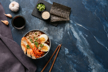 Bowl of ramen noodle soup with chicken and korean carrot salad on blue background