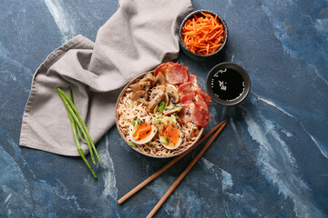 Bowl of ramen noodle soup with bacon and mushrooms on blue background