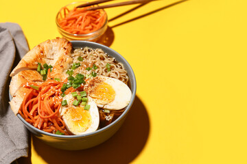 Bowl of ramen noodle soup with chicken and korean carrot salad on yellow background, closeup