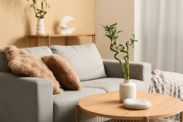 Vase with bamboo stems on wooden table and stylish sofa in living room