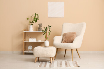 Stylish armchair, pouf, shelving unit with decor and bamboo stems near color wall