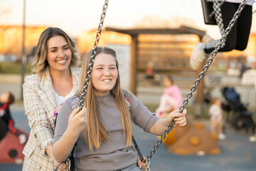 A woman smiles alongside a girl while swinging, encapsulating a moment of joy and connection during...