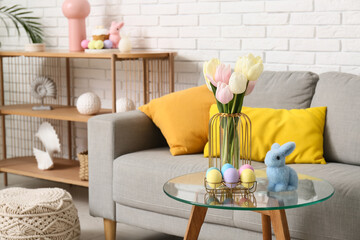 Glass coffee table with Easter eggs, bunny and tulip flowers in festive living room, closeup
