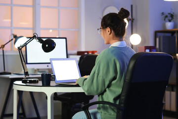Young woman working with laptop at office in evening, back view