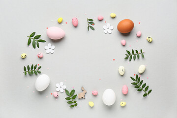 Frame made of Easter eggs, green leaves and paper flowers on grey background