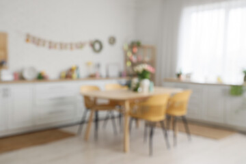 Interior of festive kitchen with tulip flowers, rabbits and Easter painted eggs on tree branches at table, blurred view
