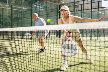 Active aged man and woman practicing Padel Tennis with other players in the tennis court outdoors