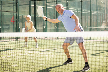 Mature sporty man playing padel game in court on sunny day