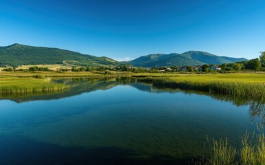 Fototapeta premium Serene Landscape with Calm Water Reflection, Lush Greenery, Rolling Hills and Clear Blue Sky in Beautiful Nature Surroundings