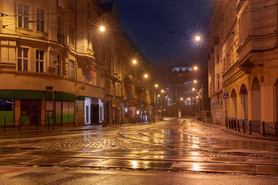 Nighttime view of a wet street in Poznan, Poland, illuminated by streetlights reflecting on the damp pavement