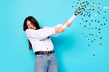 Happy woman blowing up confetti popper on light blue background. Surprise party