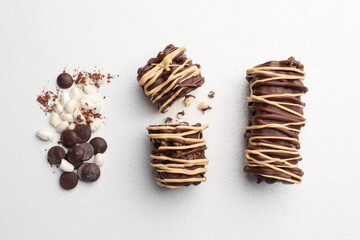 Delicious chocolate puffed rice bars and cacao chips on white table, flat lay