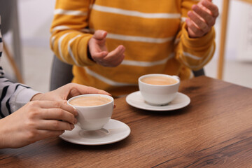 Coffee break. Women with cups of hot drinks at wooden table indoors, closeup