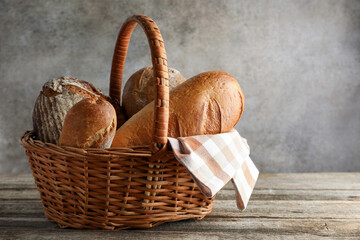 Different freshly baked bread loafs in wicker basket on wooden table, space for text