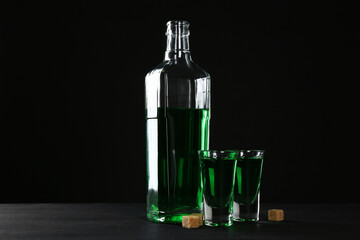 Absinthe in shot glasses, bottle and brown sugar on table against black background