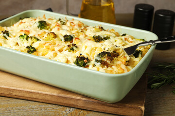 Tasty pasta casserole with cheese and broccoli in baking dish on wooden table, closeup