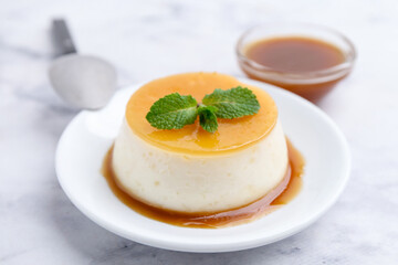 Tasty pudding with caramel sauce served on white marble table, closeup