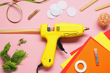 Hot glue gun and handicraft materials on pink background, flat lay