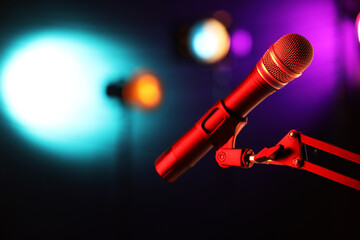 Obraz premium Microphone on stand against color background with blurred lights, space for text. Bokeh effect