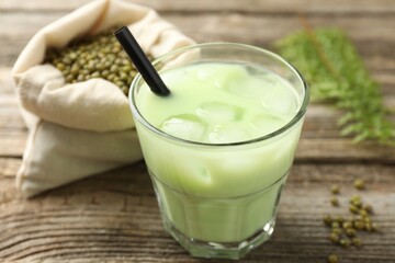Fresh mung bean juice with ice in glass and seeds on wooden table, closeup