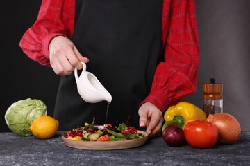 Woman pouring oil onto tasty salad at dark textured table, closeup