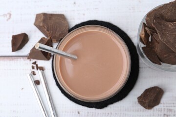 Tasty chocolate milk in glass and pieces of chocolate on white wooden table, flat lay