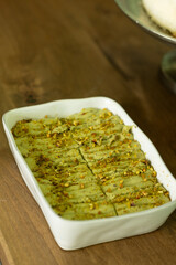 Pistachio tiramisu garnished with crushed pistachio sliced into pieces in a white ceramic dish