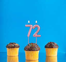 Three birthday cupcakes with number 72 candle - Blue background.