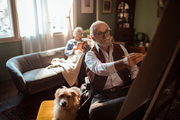 Senior male artist painting on canvas at home with dog