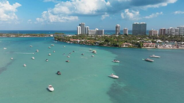 This is a stunning aerial capture of the beautiful Haulover Sandbar located in Florida, showcasing various boats and the vibrant turquoise waters against a striking urban backdrop