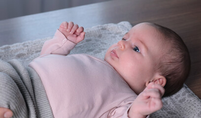 Cute newborn baby in pink bodysuit looking attentively at adult. Healthy table exercises for babies at home.