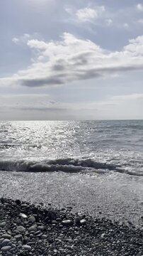 View of the calm sea, rolling waves on the pebble beach and the sky with white clouds