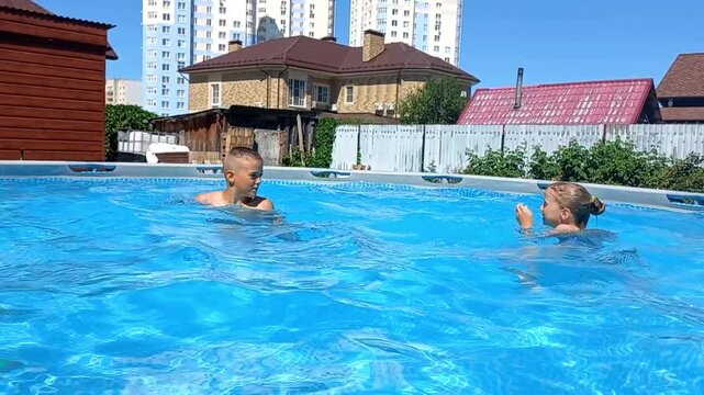 brother and sister splashing, playing in a blue pool in the summer in the yard of the house, pushing and catching each other