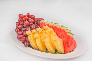 A fresh fruit platter featuring sliced watermelon, pineapple, and a bunch of red grapes, beautifully arranged on a white plate for a colorful presentation.