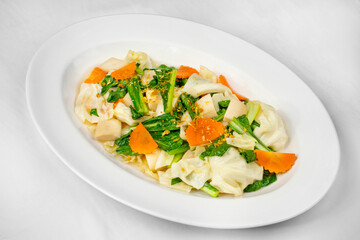 This image shows a white oval plate with stir-fried vegetables, including cabbage, leafy greens, and sliced carrots, garnished with crispy garlic or seasoning.