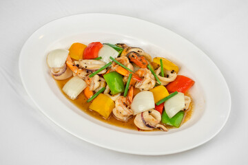 This image shows a white oval plate with stir-fried seafood, including squid and shrimp, mixed with bell peppers, onions, and green beans in a savory sauce.