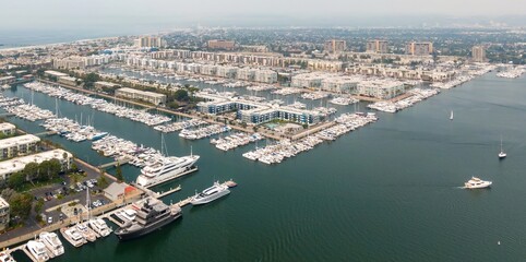 Naklejka premium Aerial view of Marina del Rey, California, USA, showcasing a dense harbor filled with yachts and boats docked along piers. Condos and buildings line the waterfront.