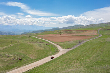 Aerial view of a red 4x4 American offroad SUV driving along a dirt road from Goghtanik through...