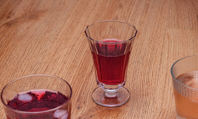 A cold, dark red drinks served in a tall. Clear glass with ice cubes. Perfect for a hot day or as a cooling accompaniment to meals. Set against a wooden background.