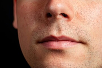 Obraz premium A close-up of a man's mouth and chin, highlighting smooth skin and subtle facial features against a dark background.