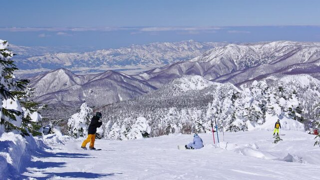 Snowboarders on a ski slope with trees and tall mountains. Yokoteyama.Handheld