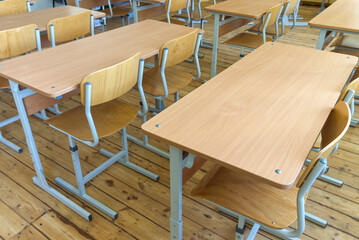 Rows of wooden desks and chairs arranged in an empty classroom on a wooden floor.