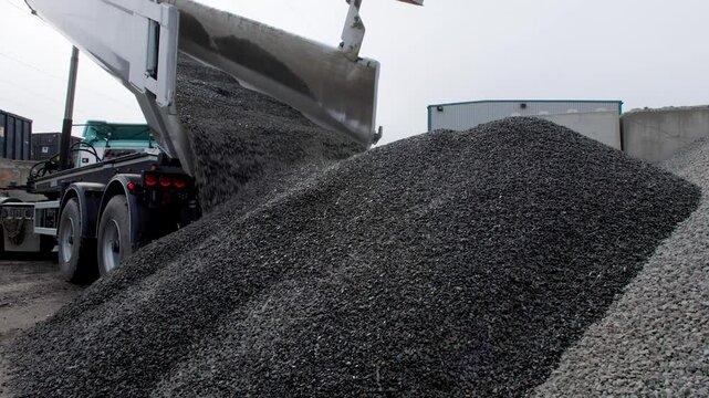 A tipper truck unloads and dumps a pile of gravel on the ground of construction site. Static shot low angle in 4k.