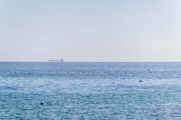 Calm blue sea with the silhouette of a large ship on the horizon